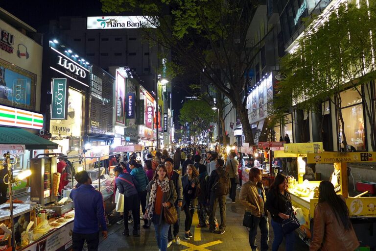 People walking between illuminated shops and street-food stalls in Myeongdong at night