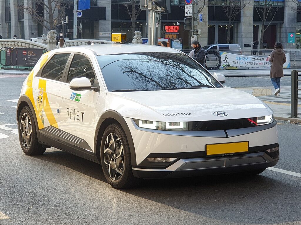 White Hyundai Ioniq 5 taxi with Kakao T branding and a yellow roof sign on a Seoul street