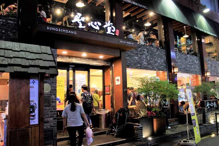 Visitors at the illuminated Sungsimdang bakery entrance in Daejeon, with an upstairs terrace